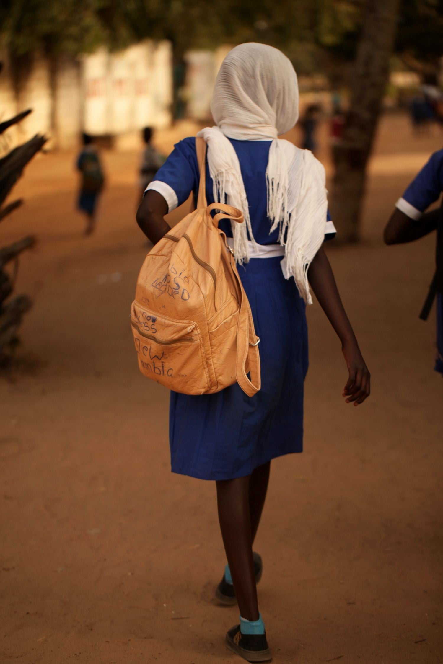 Child walking away from the camera, holding a backpack