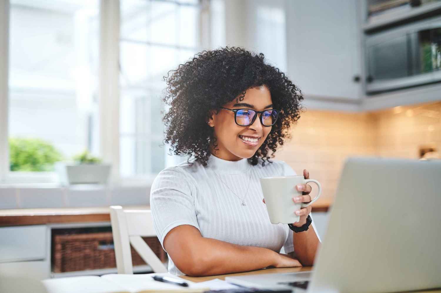 Woman holding a coffee cup and smiling at her computer