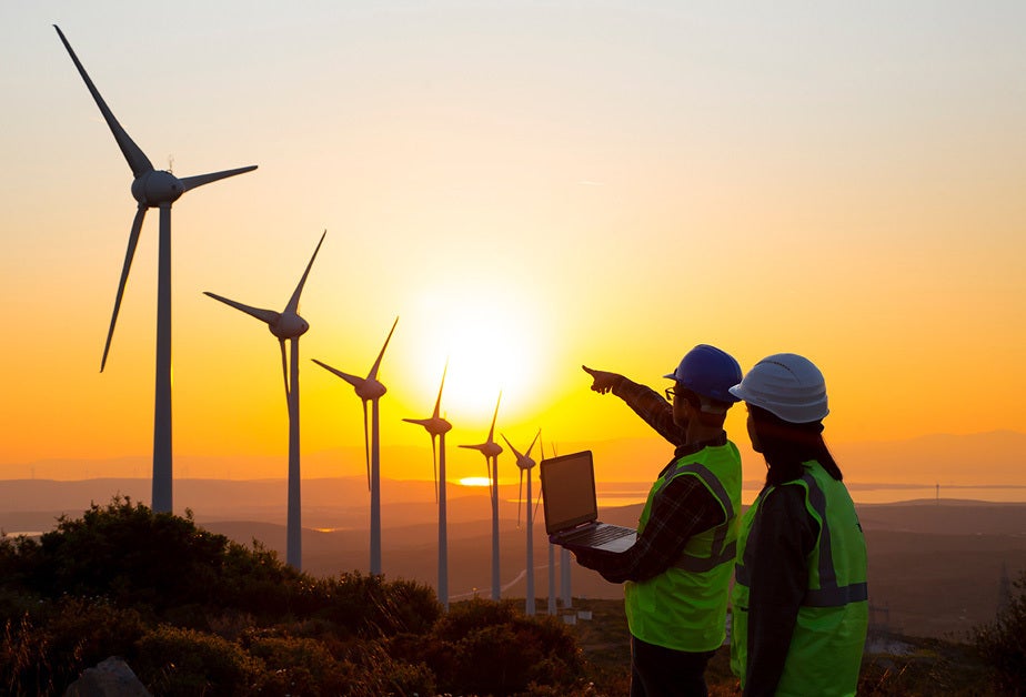 Workers in safety gear inspect wind turbines.