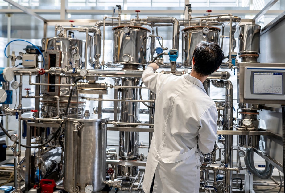 A man in a white lab coat stands in front of machinery.