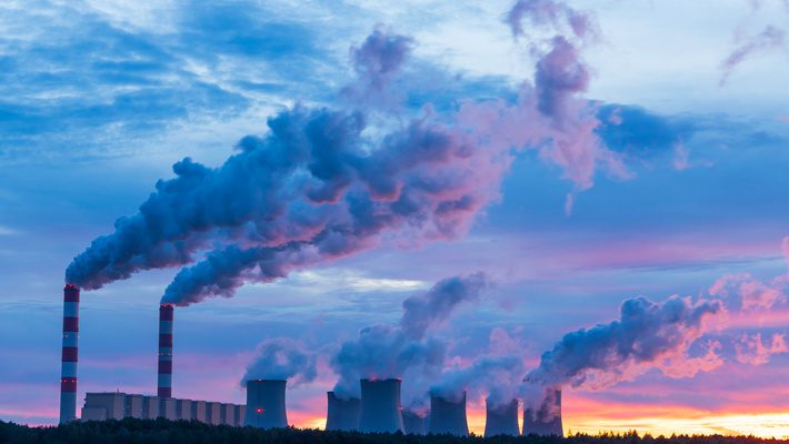 A series of smokestacks against a sunrise, representing supply chain carbon emissions.